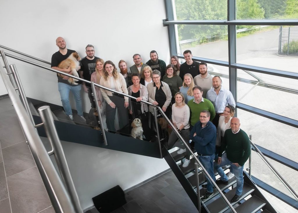 Gruppenfoto des Gisbo Teams mit Bürohunden auf einer Treppe mit Glasfront