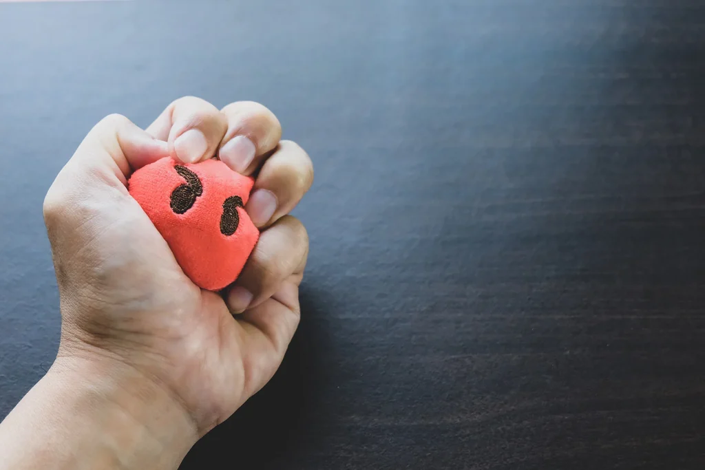 Hand drückt einen roten Stressball mit Gesicht, Motiv zum Deeskalationstraining von Gisbo
